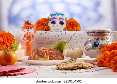 Traditional Mexican offering for the day of the dead with sweets, bread of the dead, aztec marigold flowers, a lit candle and fruit over typical minced paper.
