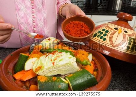 Traditional Moroccan immigrant woman in Europe adding spices to her tajine during Ramadan in her modern kitchen