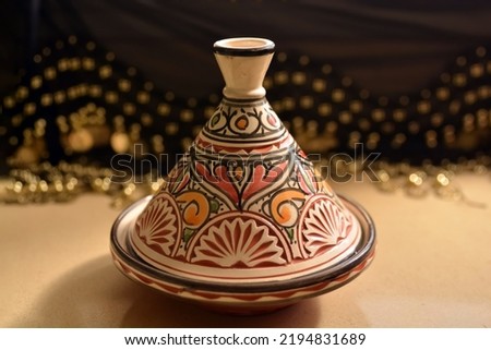 Traditional Moroccan tagine serving dish. In cream, brown, orange and green colors. On a neutral background and behind fabric with gold coins
