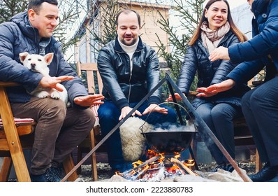 Traditional Mulled Wine With Slices Of Orange Preparing In Pot Over Burning Logs In Winter In Countryside, Friends In Winter Day