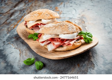 Traditional New Orleans muffaletta sandwiches with mortadella, salami and provolone cheese served in an Italian ciabatta bread as close-up on a wooden design cutting board
