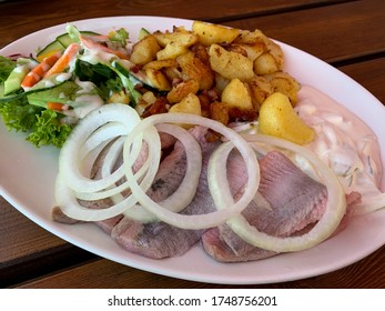 Traditional North German Dish With Marinated Herring Filet, Onion Rings, Roast Potatoes And Green Salad On The Plate Top View
