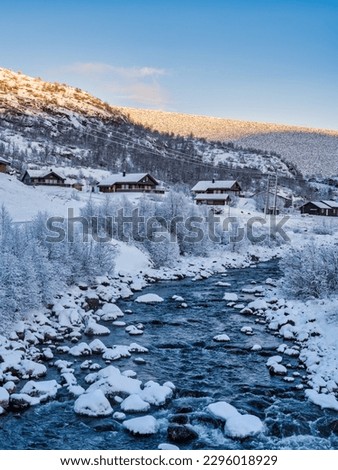 Traditional norwegen wooden houses on a river side covered in snow in Eidfjord village during sunset, Norway