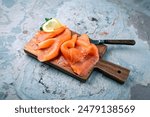 Traditional Norwegian smoked salmon in slices with parsley and lemon served as close-up on rustic wooden chopping board with text space 