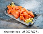 Traditional Norwegian smoked salmon in slices with lemon slices served as close-up on a Nordic design tray with text space 