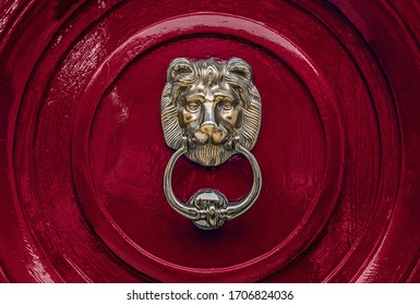 Traditional old solid brass lion head door knocker on a seamless dark red painted door.