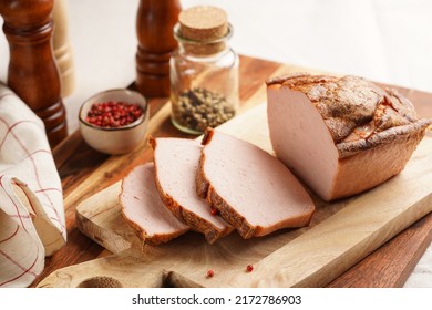 Traditional oven baked bavarian meal leberkäse sliced - meat dish made of corned beef, pork and bacon, finely ground and bakes as a bread loaf, on wooden board on dark wooden table with spices