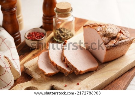 Traditional oven baked bavarian meal leberkäse sliced - meat dish made of corned beef, pork and bacon, finely ground and bakes as a bread loaf, on wooden board on dark wooden table with spices