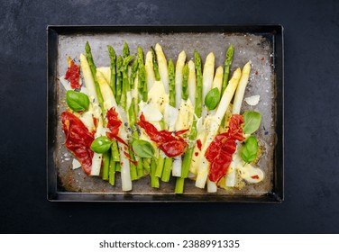 Traditional oven baked white and green asparagus with cheese, sauce hollandaise and bacon served as top view on a rustic tray  - Powered by Shutterstock