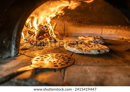 Traditional oven for baking pizza with burning wood and shovel. The cook rotates the pizza in the oven to ensure even baking.