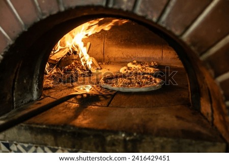 Traditional oven for baking pizza with burning wood and shovel. The cook rotates the pizza in the oven to ensure even baking.