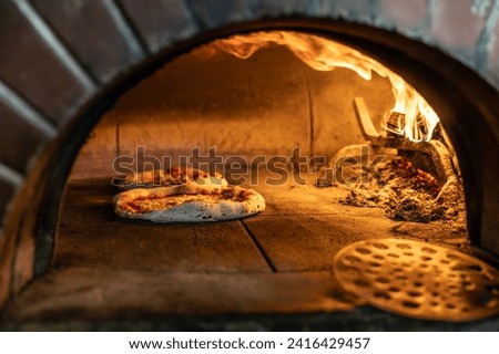 Traditional oven for baking pizza with burning wood and shovel. Several pizzas are baked in a brick oven.