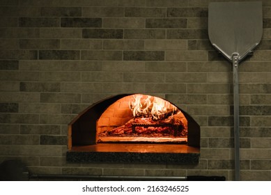 A traditional oven for cooking and baking pizza with a shovel. Firewood burning in the oven. Wood-fired oven. Image of a brick pizza oven with fire. - Shutterstock ID 2163246525