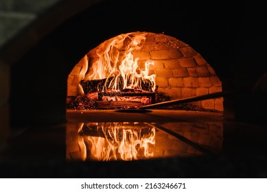 A traditional oven for cooking and baking pizza with a shovel. Firewood burning in the oven. Wood-fired oven. Image of a brick pizza oven with fire.