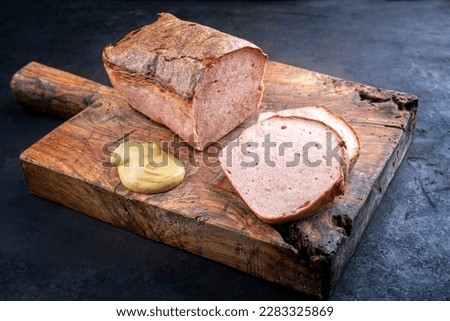 Traditional oven-fresh bavarian leberkaese sliced and as piece served spicy mustard as close-up on a rustic wooden board 