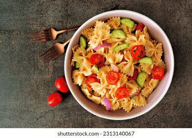 Traditional pasta salad with tomatoes, onion and cucumbers. Overhead view on a dark stone background.