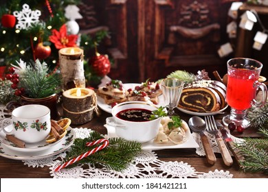traditional in Poland Christmas Eve dishes with red borscht and dumplings, herring with cranberries and poppy seed roll cake on festive table in rustic style