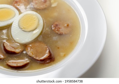 Traditional Polish Sour Soup With Sausage And Eggs In A White Deep Plate, Eastern European Meal