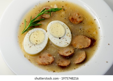 Traditional Polish Sour Soup With Sausage And Eggs In A White Deep Plate, Eastern European Meal