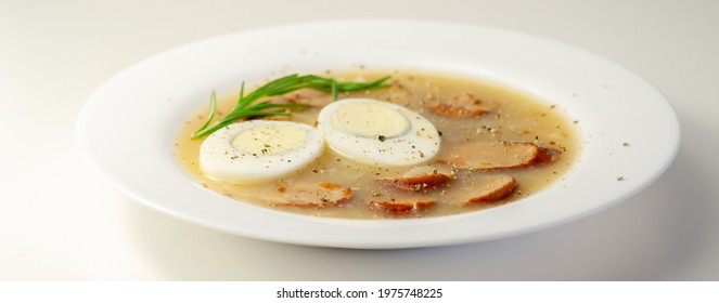 Traditional Polish Sour Soup With Sausage And Eggs In A White Deep Plate, Eastern European Meal