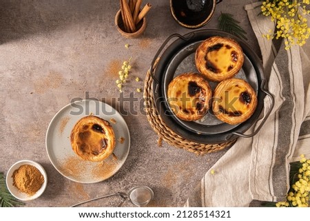 Traditional Portuguese pastry Pastel de Nata or Pastel de Belém served with cinnamon powder in a traditional tray on a rustic board. Egg tart