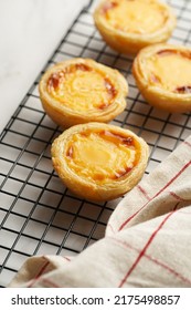 Traditional Portuguese Vanilla Pudding Puff Pastry Pastel De Nata On Black Oven Rack On Marble Background With Checkered Kitchen Towel