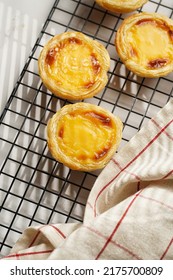 Traditional Portuguese Vanilla Pudding Puff Pastry Pastel De Nata On Black Oven Rack On Marble Background With Checkered Kitchen Towel