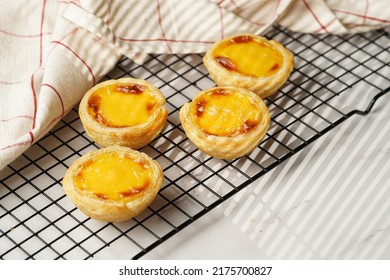 Traditional Portuguese Vanilla Pudding Puff Pastry Pastel De Nata On Black Oven Rack On Marble Background With Checkered Kitchen Towel