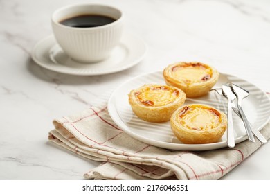 Traditional Portuguese Vanilla Pudding Puff Pastry Pastel De Nata On Black Oven Rack On White Plate On Checkered Kitchen Towel With A Cup Of Coffee In White Porcelain