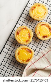 Traditional Portuguese Vanilla Pudding Puff Pastry Pastel De Nata On Black Oven Rack On Marble Background With Checkered Kitchen Towel