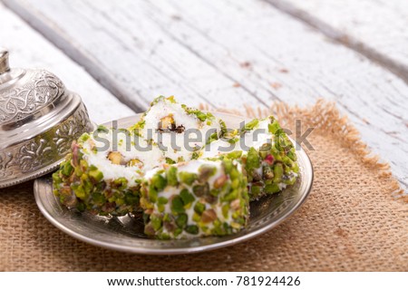 Traditional Ramadan Dessert Pistachio Turkish Delight in red napkin on rustic black wood background. Lokum or rahat and many other transliterations is a family of confections based on gel of starch.