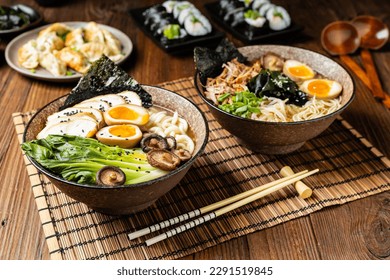 Traditional ramen with jerked pork or chicken.  With udon or ramen noodles. Served in classic bowls. Gyoza dumplings and mushrooms in the background.  Natural wooden background.
