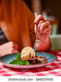 Traditional Recipe Brownie With Ice Cream Served On A Blue Plate Over Table With Red Plaid Tablecloth. Italian Cuisine Concept, Sweet Dessert. Young Woman Eating Chocolate Brownie And Ice Cream.