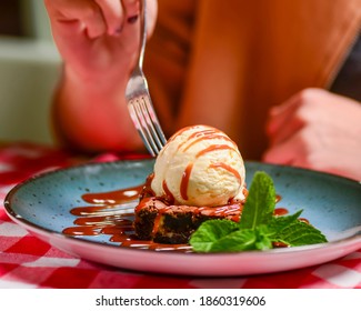 Traditional Recipe Brownie With Ice Cream Served On A Blue Plate Over Table With Red Plaid Tablecloth. Italian Cuisine Concept, Sweet Dessert. Young Woman Eating Chocolate Brownie And Ice Cream.