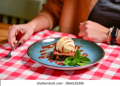 Traditional Recipe Brownie With Ice Cream Served On A Blue Plate Over Table With Red Plaid Tablecloth. Italian Cuisine Concept, Sweet Dessert. Young Woman Eating Chocolate Brownie And Ice Cream.