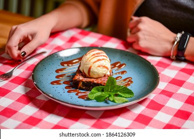 Traditional Recipe Brownie With Ice Cream Served On A Blue Plate Over Table With Red Plaid Tablecloth. Italian Cuisine Concept, Sweet Dessert. Young Woman Eating Chocolate Brownie And Ice Cream.