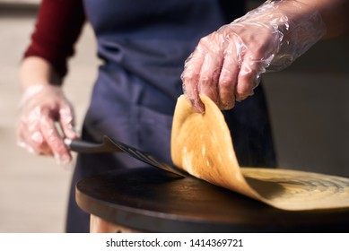 Traditional Recipe For Cooking Big Crepes. Chef Hands In Disposable Gloves Turn Over Big Hot Pancake With Spatula On Portable Round Cooktop While Baking Process. Blurred Background. Focus Macro View.