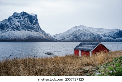 Traditional red Norwegian cabin by a tranquil fjord, framed by a dramatic snow-capped mountain in the background. A perfect depiction of serene Scandinavian nature and rustic charm - Powered by Shutterstock