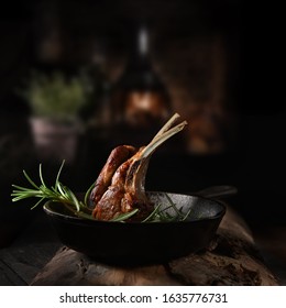 Traditional, roasted rack of lamb cutlets in a wrought iron skillet with rosemary herbs shot against a dark, rustic background with generous accommodation for copy space.