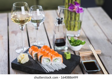Traditional roll with red fish on a stone board with wine, sauces, vasabi on a table in a restaurant. Japanese food. Seafood on the table in a restaurant. Beautiful serving and creative decoration.