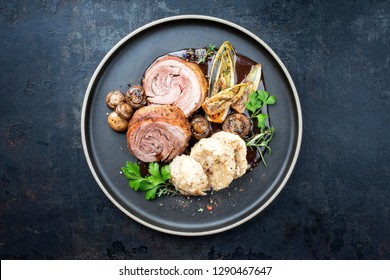 Traditional rolled boar roast with dumpling, fried vegetable and mushroom as top view on a modern design plate with game red wine sauce