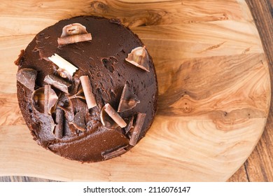 Traditional Round Chocolate Cake With White And Dark Chocolate Shavings Or Chips On Top. Bakery Product On A Wooden Board And Table. Birthday Cake. Top Down View.