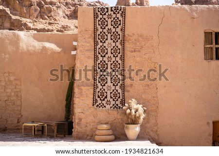 Traditional Rug and a Wicker Floor for Serving Food Hanging on an Old Mud Wall in 