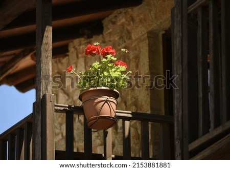 Traditional rural house wooden balcony railing with a handmade clay pot and red geraniums in Platanos, Arcadia Peloponnese, Greece.