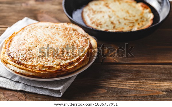 Traditional\
Russian Crepes Blini stacked in a plate and pancake in a cast-iron\
frying pan on dark wooden table. Maslenitsa traditional Russian\
festival meal. Russian food, russian\
kitchen