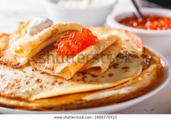 Traditional Russian Crepes Blini stacked in a plate\
with red caviar, fresh sour cream on light background. Maslenitsa\
traditional Russian festival meal. Russian food, russian kitchen.\
Close up.