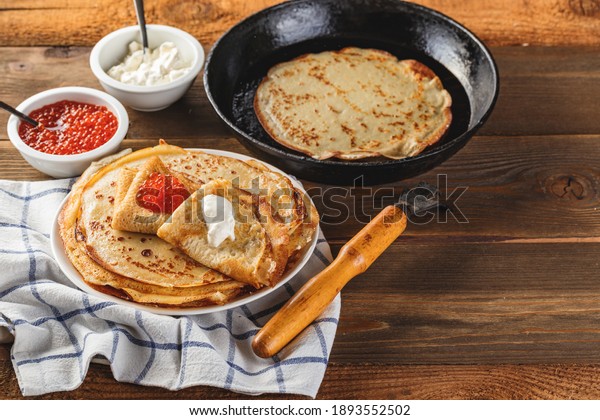 Traditional Russian\
Crepes Blini stacked in a plate with red caviar, fresh sour creamon\
dark wooden table. Maslenitsa traditional Russian festival meal.\
Russian food, russian\
kitchen