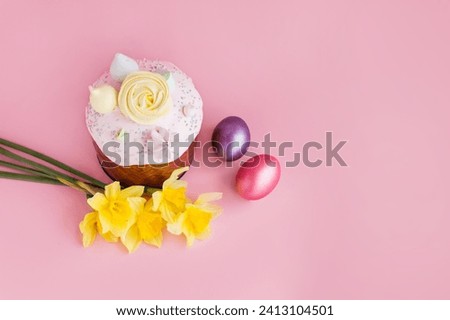 Traditional russian Easter ortodox cake with daffodil flower and colorful eggs on light pink background. Kulic, Kulich, Paska homemade bread with glaze. Spring christian holiday. Festive celebration