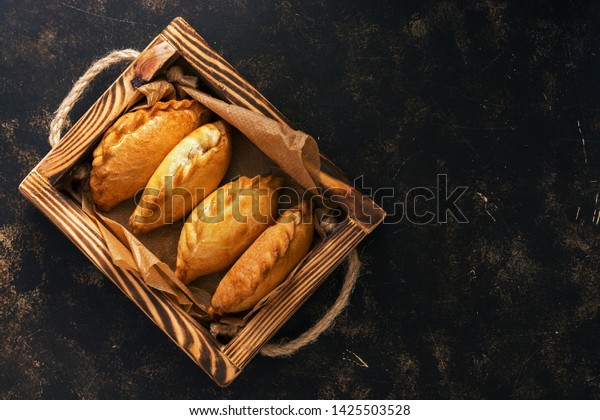 Traditional Russian pies in a wooden tray on a dark\
rustic background. Russian pirozhki ,baked patties. Top view, copy\
space, flat lay