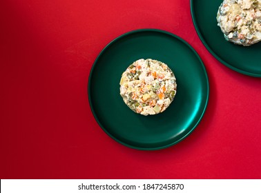 Traditional Russian salad called Olivier served on a green plate on a red background. Festive salad of meat and vegetables. Concept for a Christmas or New Year dinner. Top view. Copy space